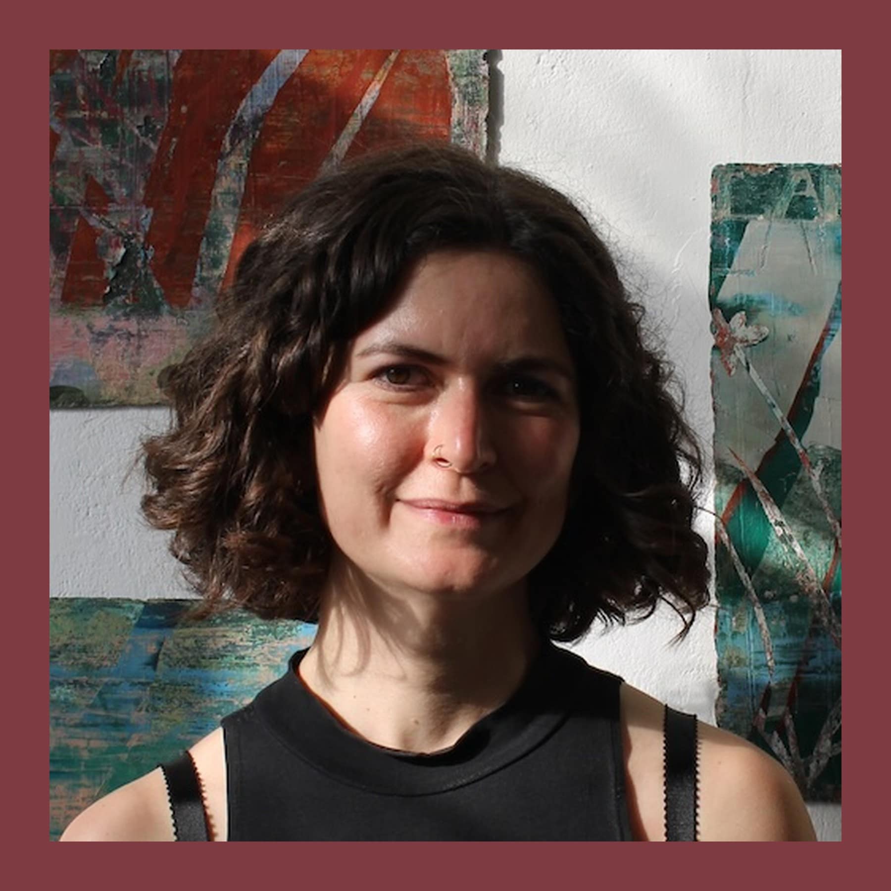 Megan Rea, with curly dark hair and a black top, in front of her scraped red and green paintings on handmade paper