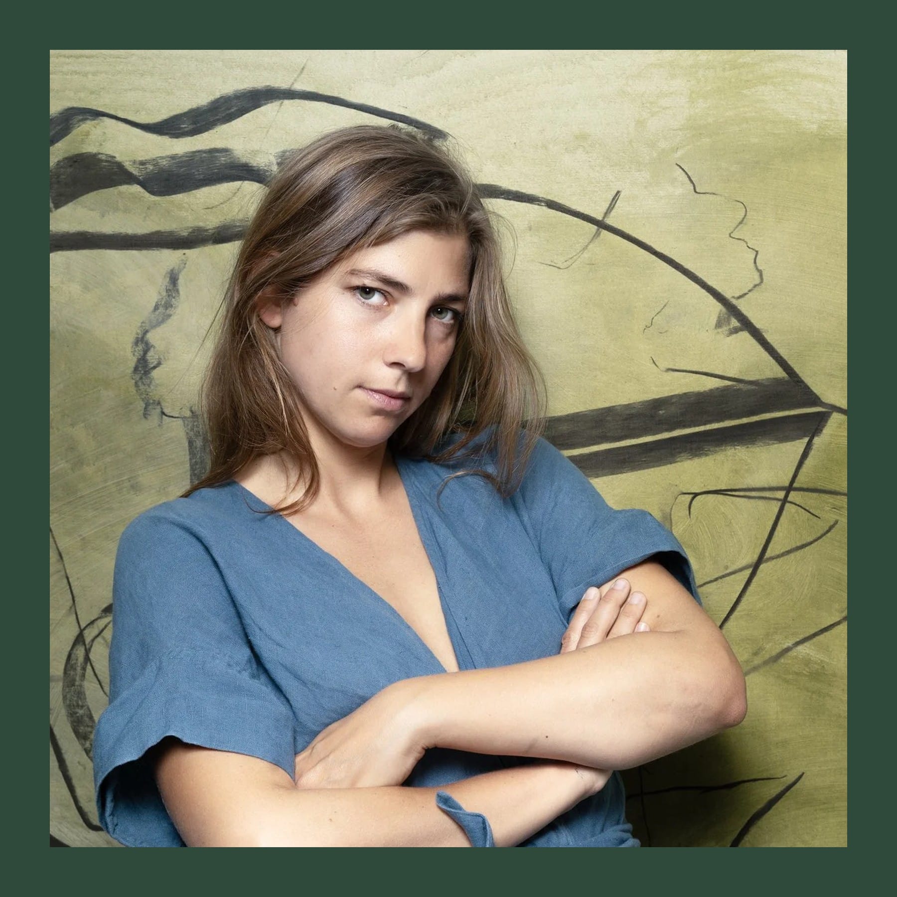 Anna Pakosz in a blue linen dress, arms folded, in front of one of her large green and black paintings