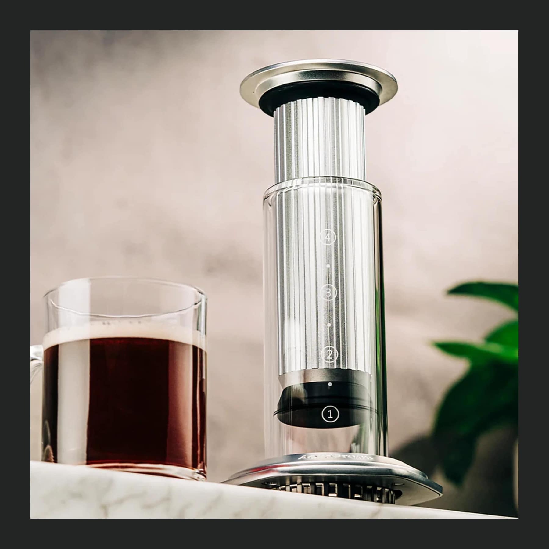 AeroPress Premium coffee maker with a glass chamber and aluminium plunger next to a glass mug of black coffee