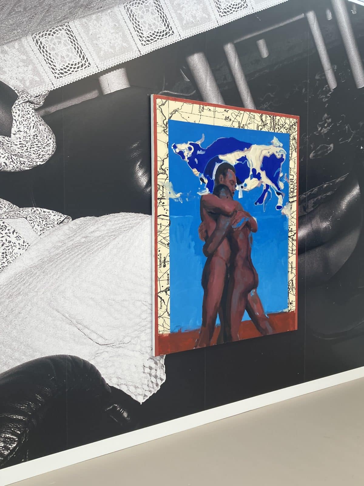 Kudzanai-Violet Hwami painting of two embracing men under a blue cow, on photographic wallpaper