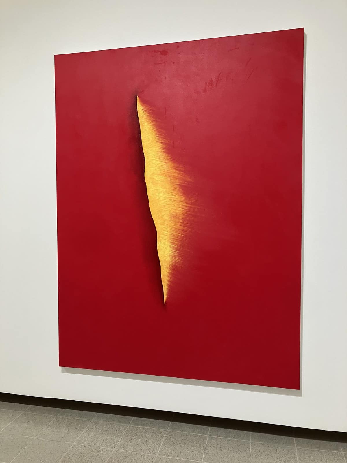 Red canvas with a single vertical gold slit, by Anish Kapoor, on a white gallery wall