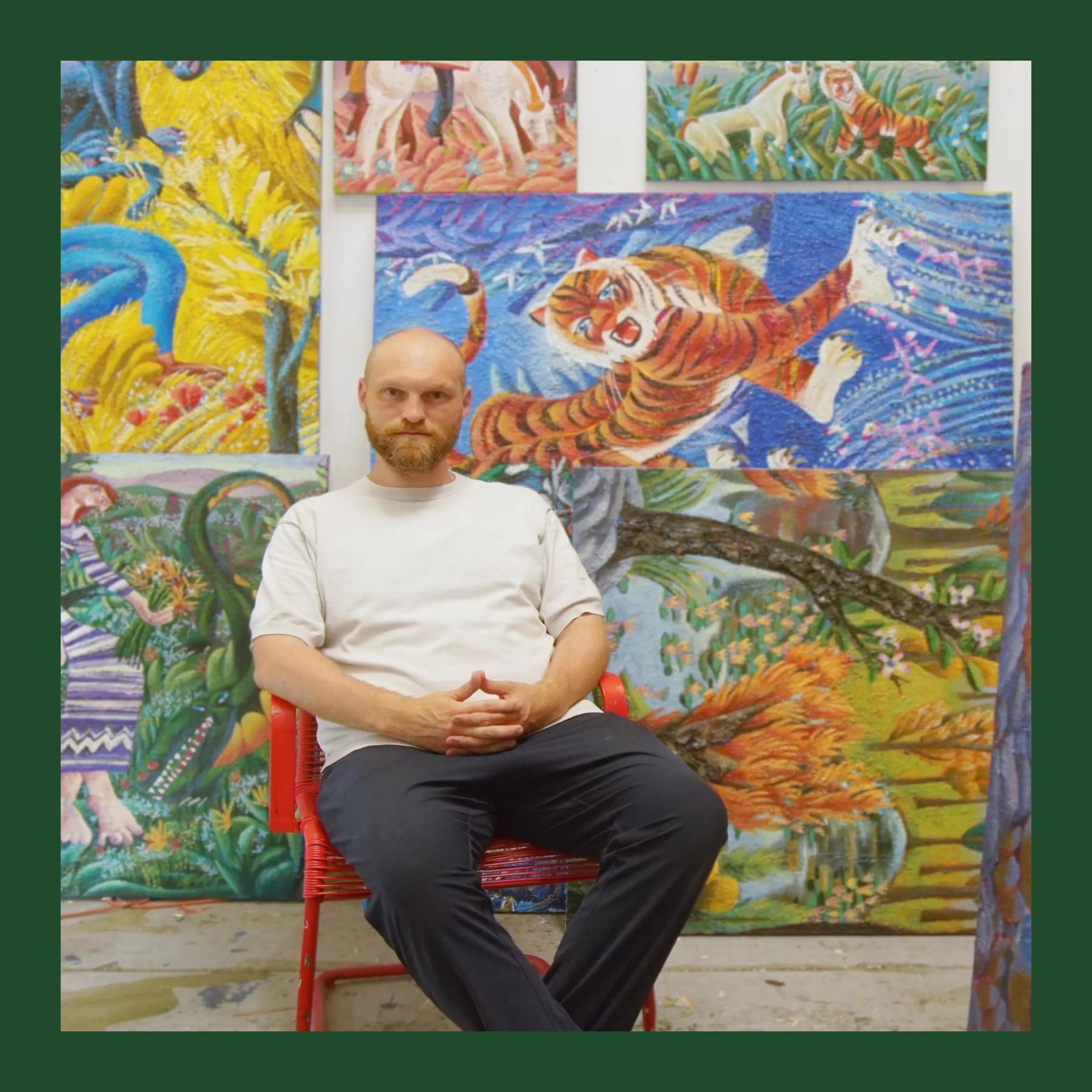Ralf Kokke sitting on a red chair in his studio, surrounded by his bright paintings of tigers, horses and figures