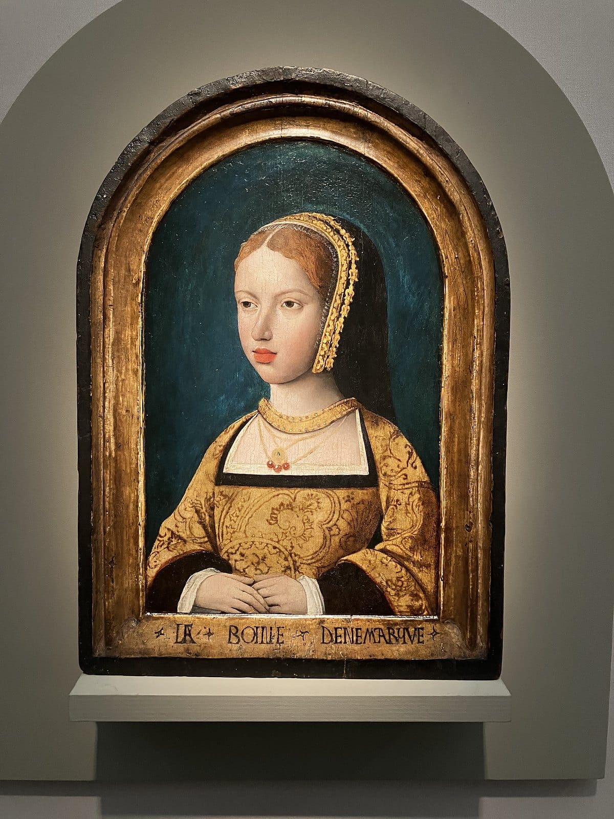 Arched oak panel portrait of a young woman in a gold gown and headdress, the frame inscribed La Roine Denemarqve