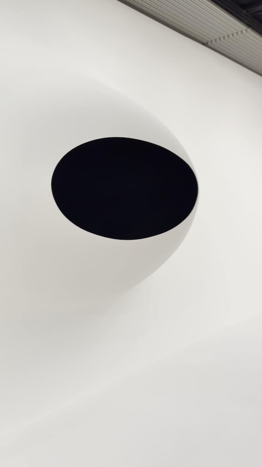 Black oval on a white wall, seen from the side so the bowl shape of the Vantablack work shows