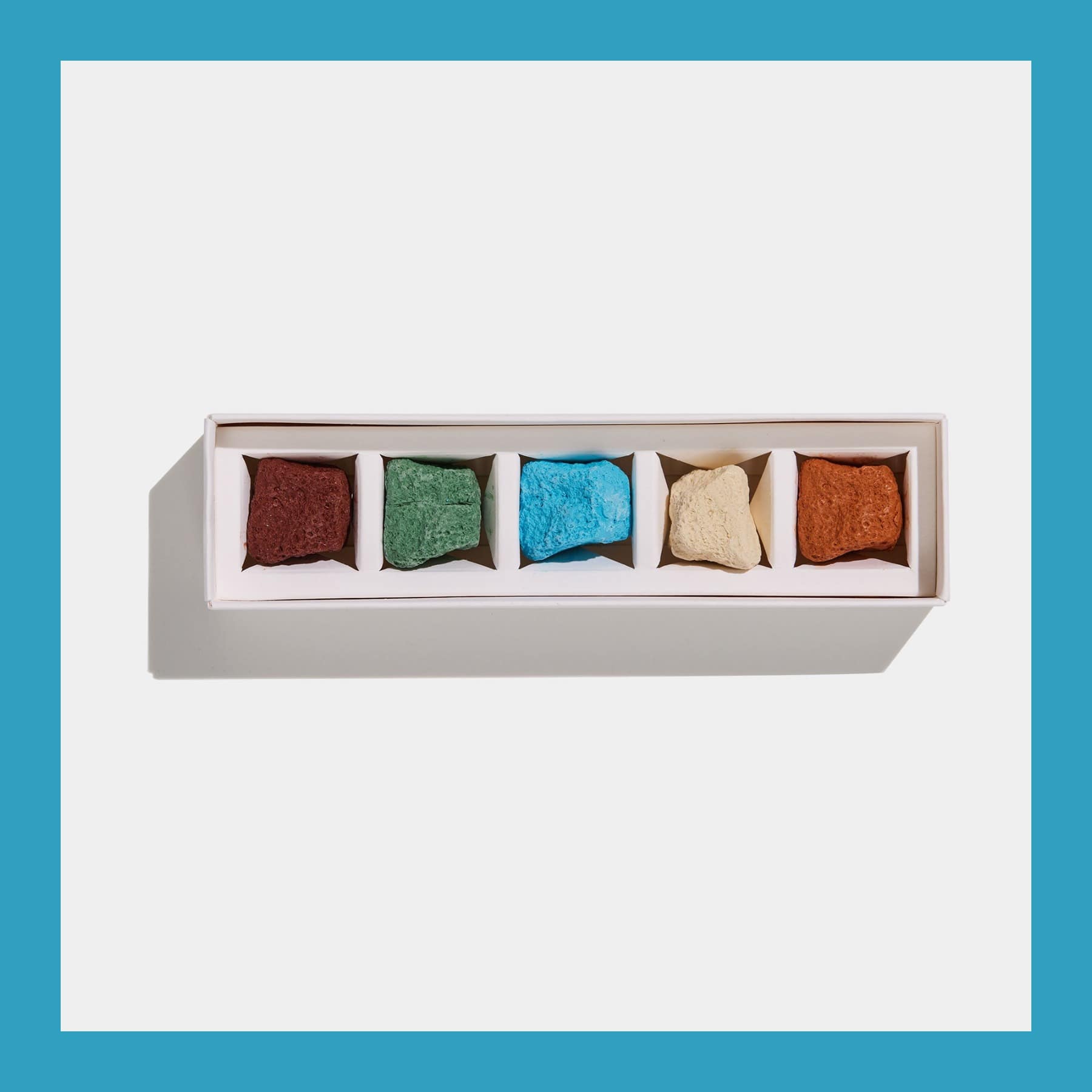 Open box of five Odujej Mudle Mini crayons shaped like pebbles in brown, green, blue, cream and orange