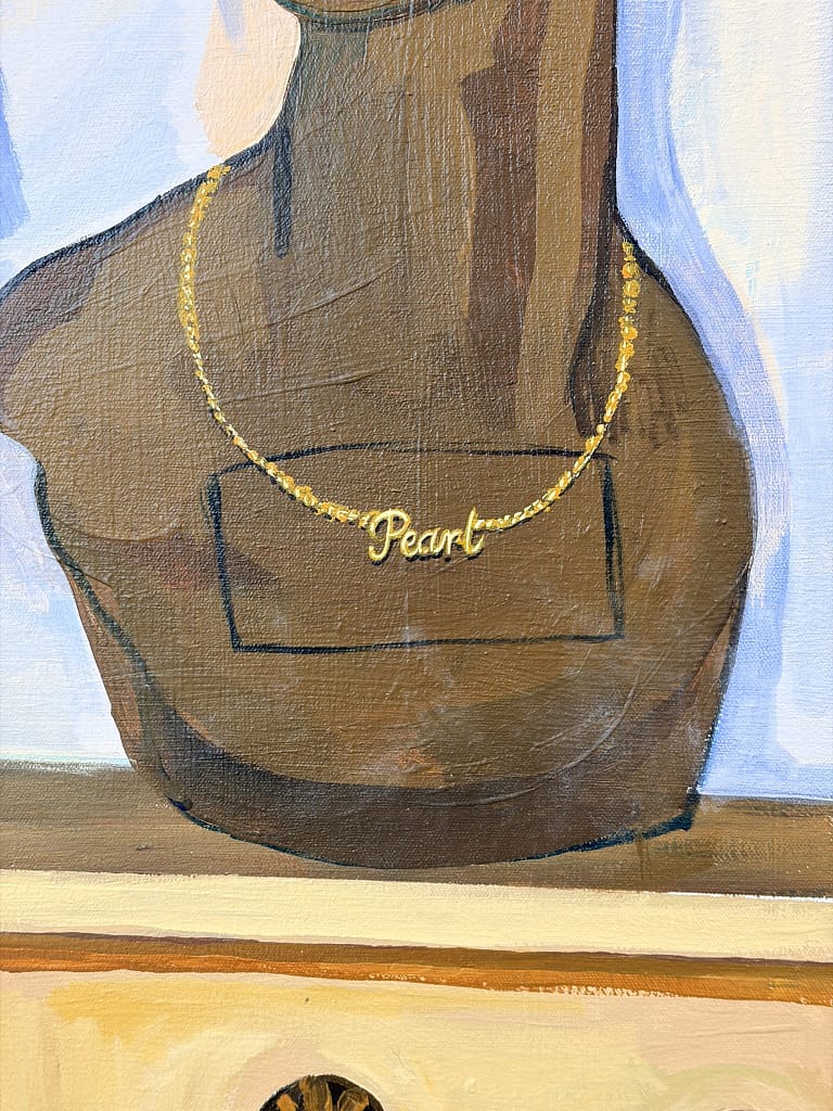 Close-up of a painted gold necklace reading Pearl on a brown mannequin bust