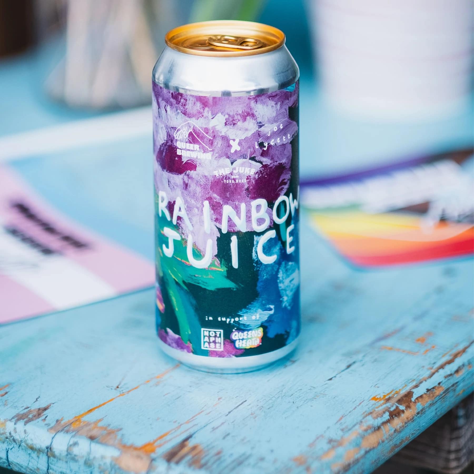 Colourful can of Queer Brewing Rainbow Juice hazy pale ale sitting on a distressed blue table