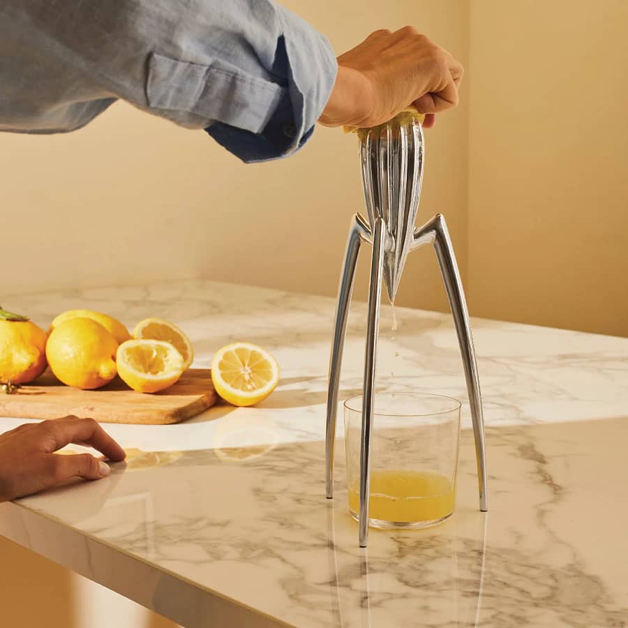 The Juicy Salif lemon squeezer by Philippe Starck in action, squeezing fresh lemon juice into a glass on a marble countertop. A stylish and functional gift for designers or first-time homeowners