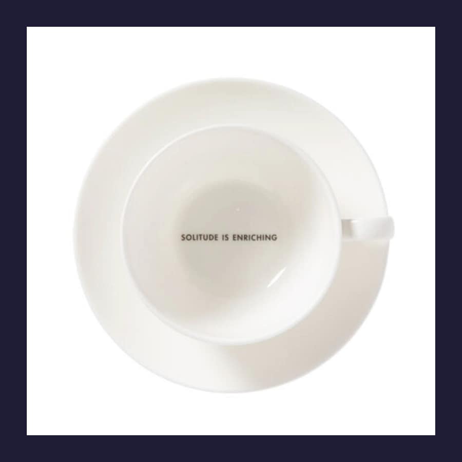 White bone china teacup and saucer with Solitude Is Enriching printed inside, viewed from above