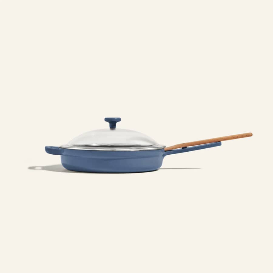 The Our Place Always Pan in blue with a wooden handle and glass lid, showcasing its stylish design and versatile functionality. Get £20 off your first order over £100 using our referral link.