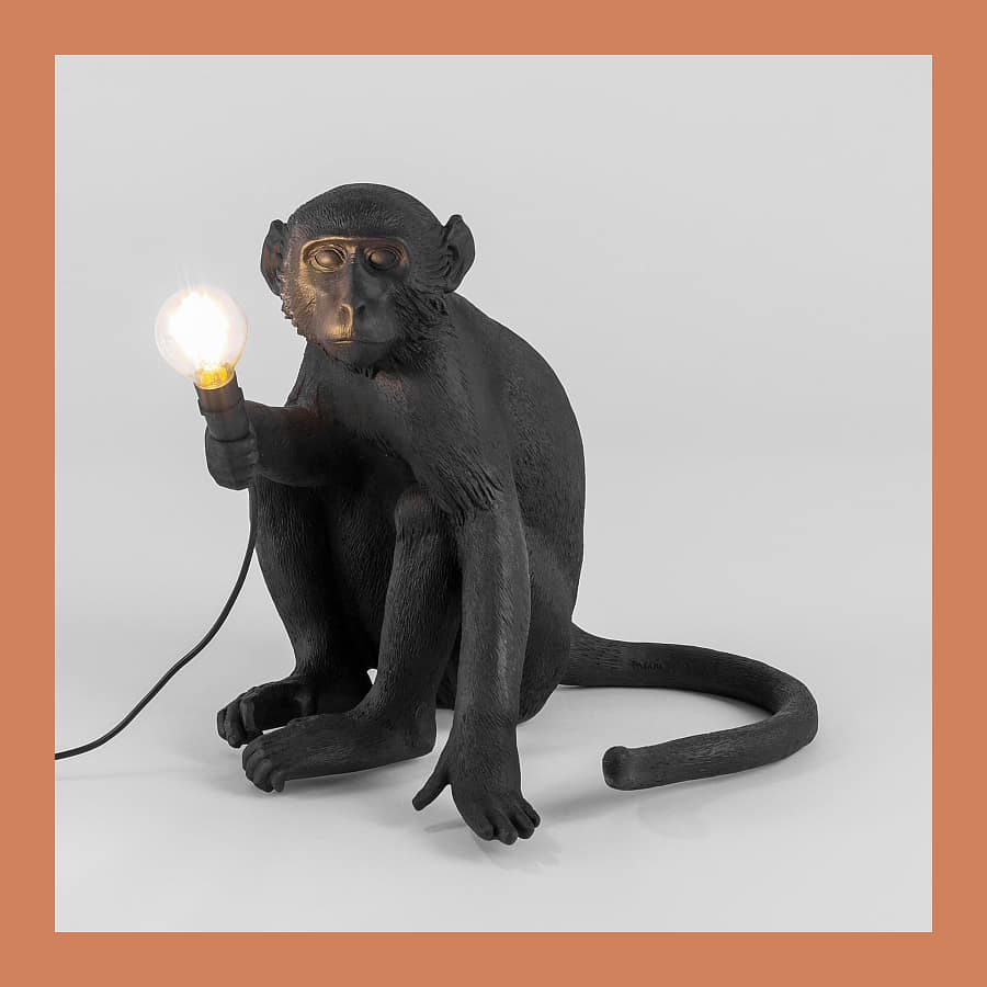 Seletti Monkey Lamp in black resin, sitting version, holding a lit bulb