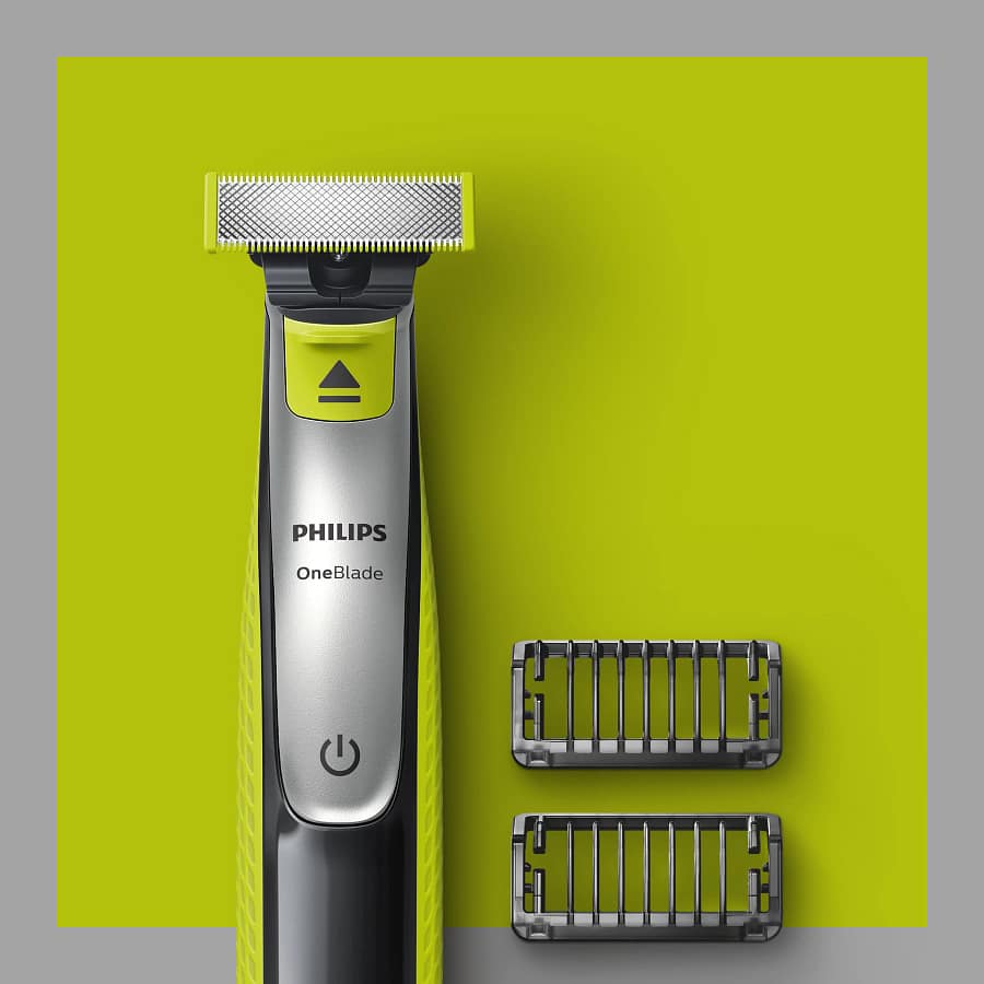 Close-up of the Philips OneBlade electric trimmer with two comb attachments on a lime green background