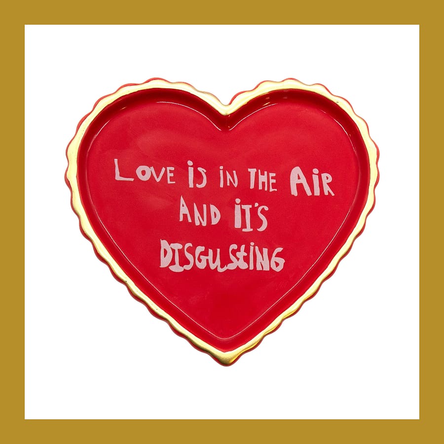 Red heart-shaped ceramic trinket tray with a gold rim, hand lettered Love is in the Air and it's Disgusting