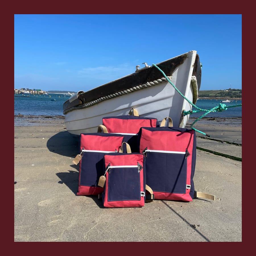 Three red and navy Rat Bags Ratpacks on the beach beside a boat on the Isles of Scilly