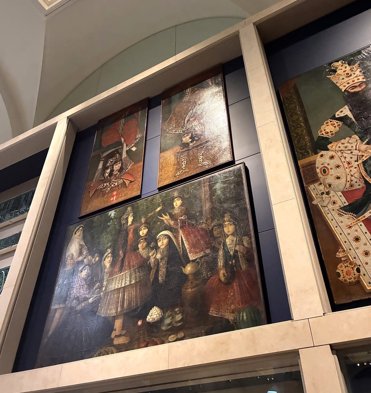 Qajar Persian oil paintings hung high in the V&A Jameel Gallery, including a group of performers and a jewelled royal portrait